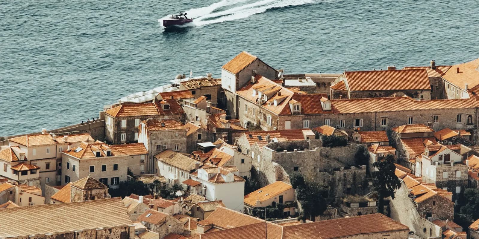 The terracotta roofs of Dubrovnik old town from above, with a boat crossing the Adriatic behind them