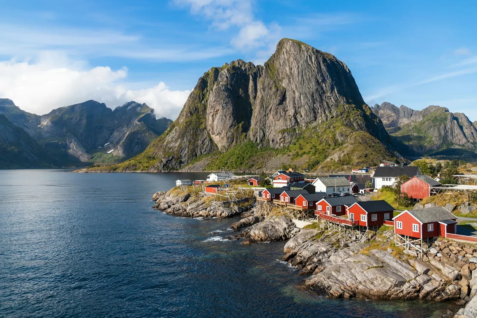 Red rorbu cabins on the rocks at Hamnoy in Lofoten with a granite peak behind them